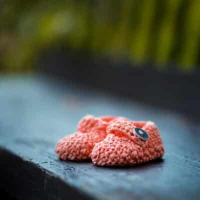 pair of baby's pink knit shoes on bench