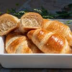 a white dish filled with croissants sitting on top of a table