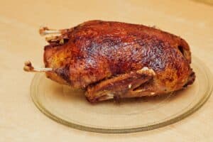 Fresh baked duck with a golden-red crust, spices and fragrant spices, lying on a glass stand right on the kitchen table. Close-up photo of the mouthwatering bird for a website, design, and culinary portal