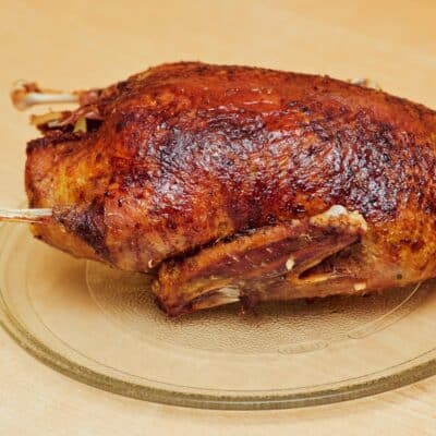 Fresh baked duck with a golden-red crust, spices and fragrant spices, lying on a glass stand right on the kitchen table. Close-up photo of the mouthwatering bird for a website, design, and culinary portal