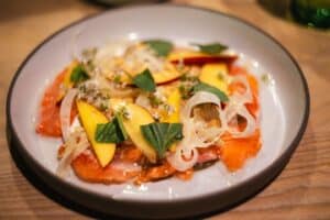 Salmon carpaccio with mango, sliced onions, and fresh herbs.