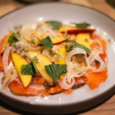 Salmon carpaccio with mango, sliced onions, and fresh herbs.