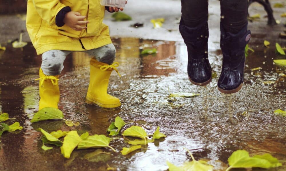 Deux enfants en bottes de pluie en caoutchouc sautant dans une flaque parsemée de feuilles d’automne