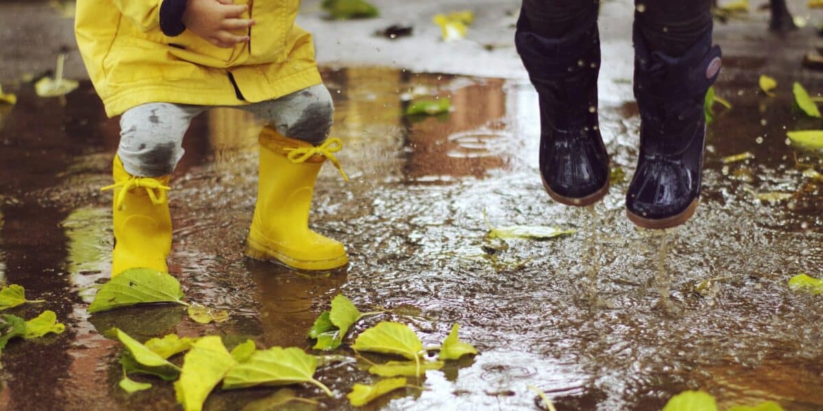 Deux enfants en bottes de pluie en caoutchouc sautant dans une flaque parsemée de feuilles d’automne