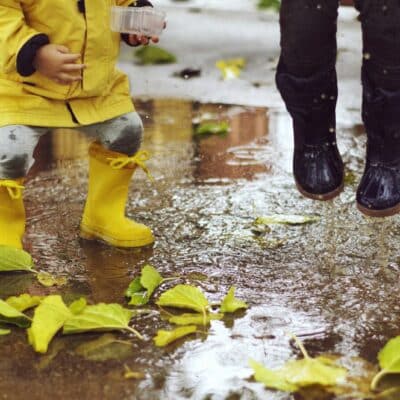 Deux enfants en bottes de pluie en caoutchouc sautant dans une flaque parsemée de feuilles d’automne